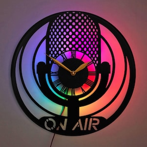 May include: A black and gold microphone-shaped clock with a rainbow LED light behind it. The clock face has Roman numerals and the words "ON AIR" are printed below the clock face.