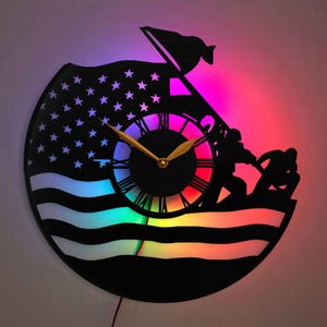 May include: A black and white vinyl record clock with a rainbow LED light effect. The clock features a silhouette of a soldier saluting the American flag.