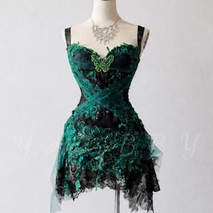 May include: A sleeveless dress on a mannequin featuring a dark green and black layered lace bodice with a sweetheart neckline. The dress is adorned with a prominent green butterfly embellishment at the center chest and a textured, uneven hemline.