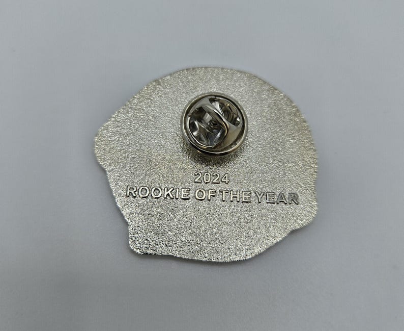 Puede incluir: Pin plateado con la inscripci&oacute;n "2024 Rookie of the Year". El pin tiene una superficie texturizada y un cierre de pin.