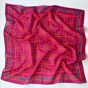 May include: A square scarf in a vibrant magenta hue featuring a repeating geometric pattern of intersecting orange lines and dark blue rectangular accents. The text KNOT-A-SQUARE is printed in the bottom right corner of the fabric design.