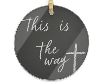 May include: Circular, dark grey ornament with the words "This is the way" in white script, and a white cross. A gold ribbon is attached for hanging. The ornament has a chalkboard-like appearance.