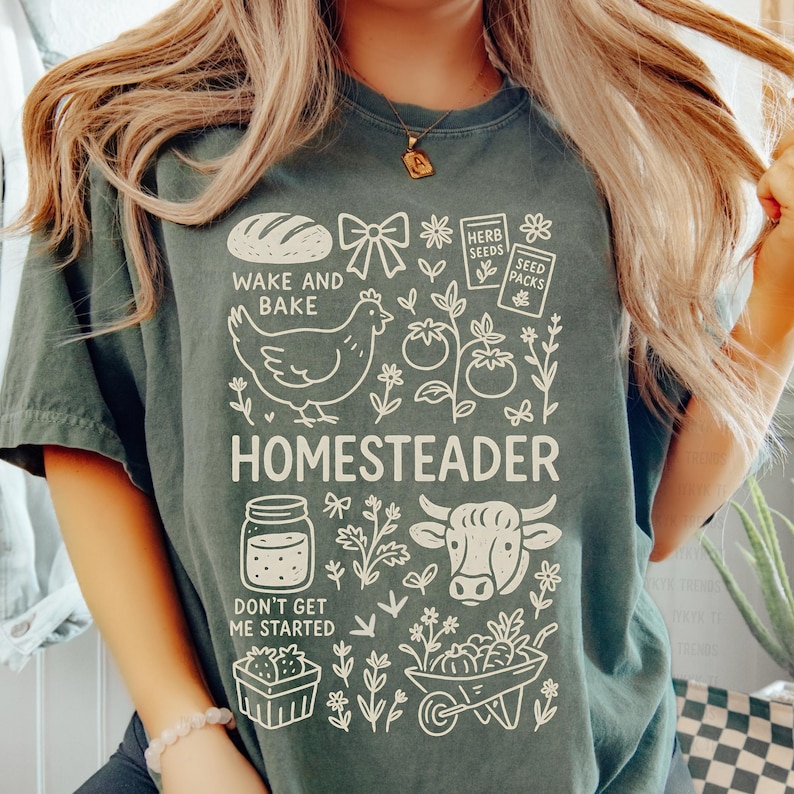 May include: A dark green t-shirt with a white graphic design featuring a loaf of bread, a chicken, tomatoes, and the word "HOMESTEADER". The text "WAKE AND BAKE" and "DON'T GET ME STARTED" are also included in the design.