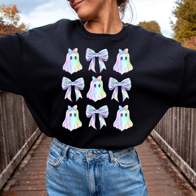 Puede incluir: Sudadera negra con un patr&oacute;n repetido de fantasmas iridiscentes que llevan lazos. Los fantasmas son de color azul claro, rosa y morado.