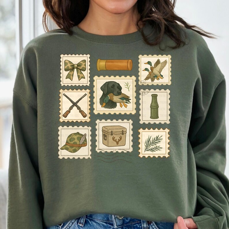 May include: Green sweatshirt featuring a collection of vintage-style postage stamps. The stamps depict hunting-themed illustrations, including a bow, shotgun shells, ducks, a dog with a duck, crossed rifles, a hat, a cooler, a bottle, and foliage.