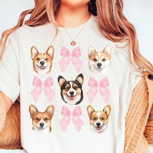May include: A white t-shirt with a pattern of six corgi dog faces with pink bows. The corgis are all facing forward and have happy expressions.