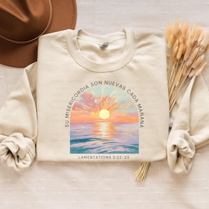 May include: A beige sweatshirt with a sunrise graphic and the text "Su misericordia son nuevas cada mañana" and "Lamentations 3:22-23".