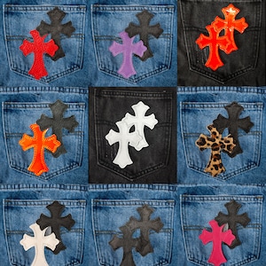 Può includere: Nove patch in pelle a forma di croce di diversi colori su tasche di jeans. I patch sono di vari colori, tra cui rosso, bianco, nero, viola, rosa e stampa leopardata.