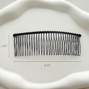 May include: Black metal hair comb with a wavy design. The comb is 4.52 inches long and 1.37 inches wide.