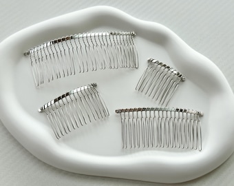 May include: Four silver hair combs on a white surface. The combs are different sizes and have a curved shape.