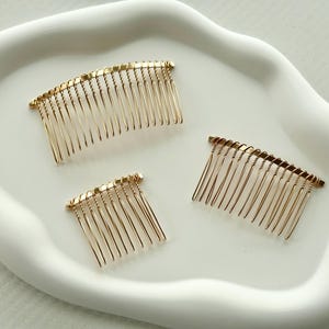 May include: Three gold hair combs of different sizes on a white surface. The combs have a twisted wire design.