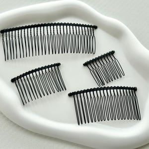 May include: Four black metal hair combs on a white surface. The combs are different sizes and have a curved shape.