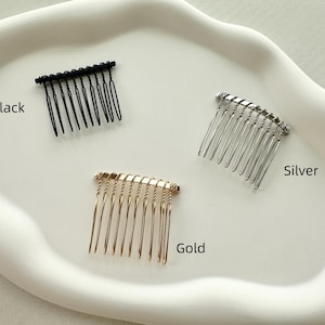 May include: Three hair combs in different colors: black, silver, and gold. The combs are all the same size and shape, with a curved design and fine teeth.