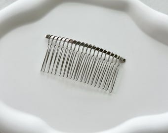 May include: A silver metal comb with a curved shape and a row of teeth. The comb is designed for styling hair.