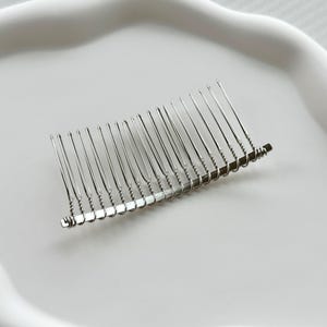 May include: A silver hair comb with a curved shape and a row of teeth. The comb is made of metal and has a shiny finish.