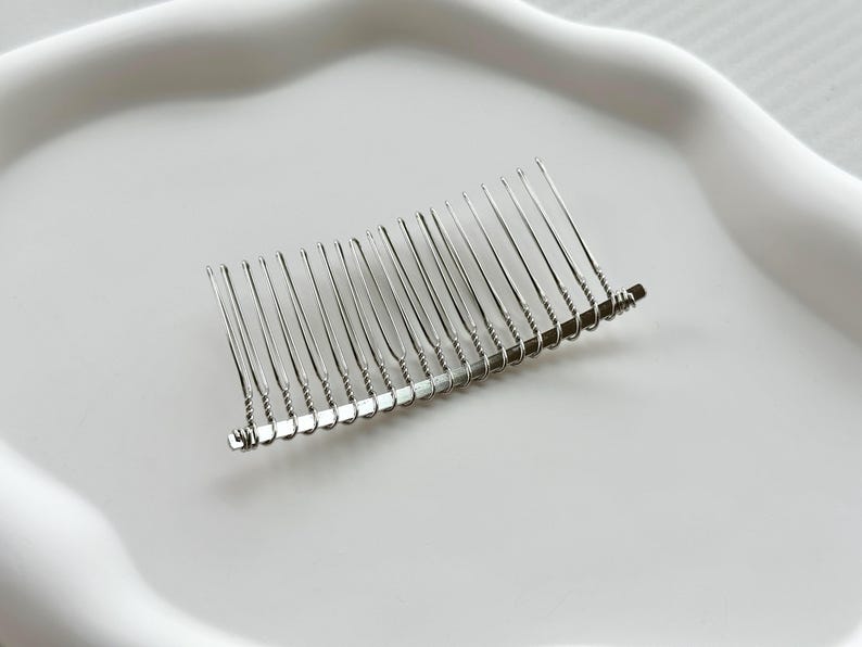 May include: A silver hair comb with a curved shape and a row of teeth. The comb is made of metal and has a shiny finish.