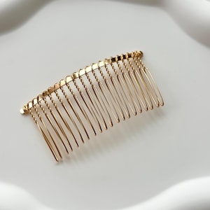 Può includere: Un pettine per capelli dorato con un design a filo intrecciato e più denti.