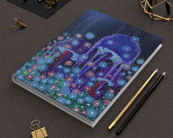 May include: A rectangular notebook featuring a dark blue cover with a painted illustration of glowing purple and blue mushrooms surrounded by small, luminous circular lights. The notebook is positioned next to two pencils and gold binder clips.
