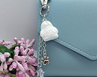 May include: A white fuzzy charm with a silver chain and a paw print charm attached to a light blue wallet.