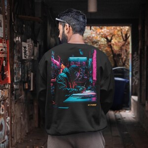 May include: Black sweatshirt with a neon-themed graphic of a person writing in a futuristic city. The design uses blue, pink, and green hues, with the word "brandes" printed at the bottom. The sweatshirt is worn by a person.