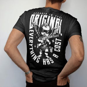 Puede incluir: Camiseta negra con un gr&aacute;fico blanco de un &aacute;ngel sosteniendo una ametralladora. El texto de la camiseta dice "BRANDED IN TYPE ORIGINAL EVERYTHING HAS A COST" y "NOT FOR THE WEAK".