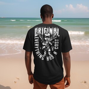 Puede incluir: Camiseta negra con un gr&aacute;fico de un &aacute;ngel sosteniendo un rifle, con las alas extendidas, y el texto "ORIGINAL EVERYTHING HAS A COST". La camiseta es de tipo "branded" y tiene un dise&ntilde;o &uacute;nico.