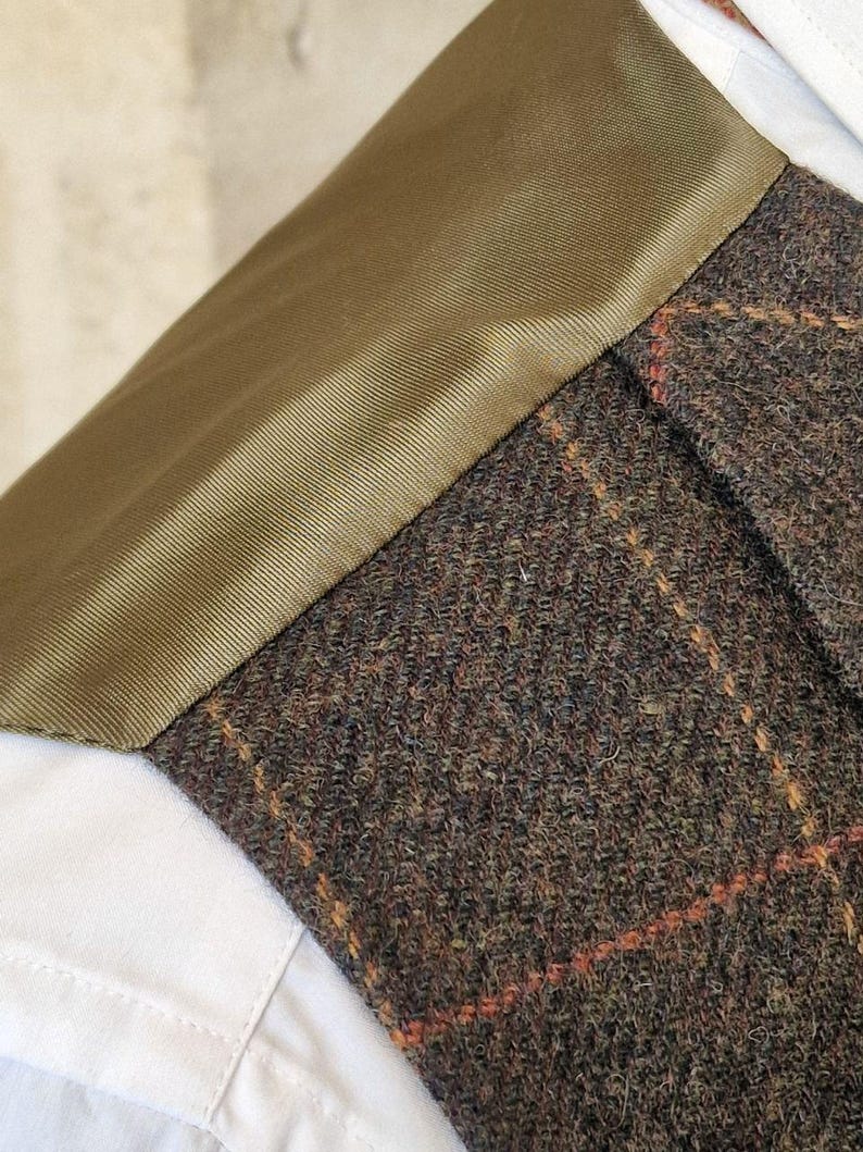 K&ouml;nnte beinhalten: Nahaufnahme eines Tweed-Jackenkragen mit braun-orangefarbenem Karomuster. Der Kragen ist mit olivgr&uuml;nem Stoff besetzt und sitzt auf einem wei&szlig;en Hemd.