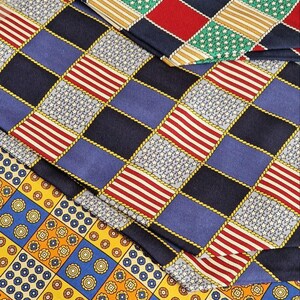 May include: Close-up of several patterned neckties. The ties feature a variety of designs, including red and white stripes, blue and white stars, and geometric patterns in yellow, blue, and red. The ties are arranged in a layered fashion.