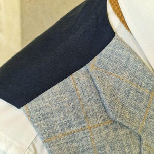 K&ouml;nnte beinhalten: Nahaufnahme eines hellblauen Tweed-Blazers mit gelbem Karomuster. Der Blazer ist &uuml;ber einem wei&szlig;en Hemd und einer marineblauen Jacke getragen. Ein hellbrauner Kragen ist sichtbar.