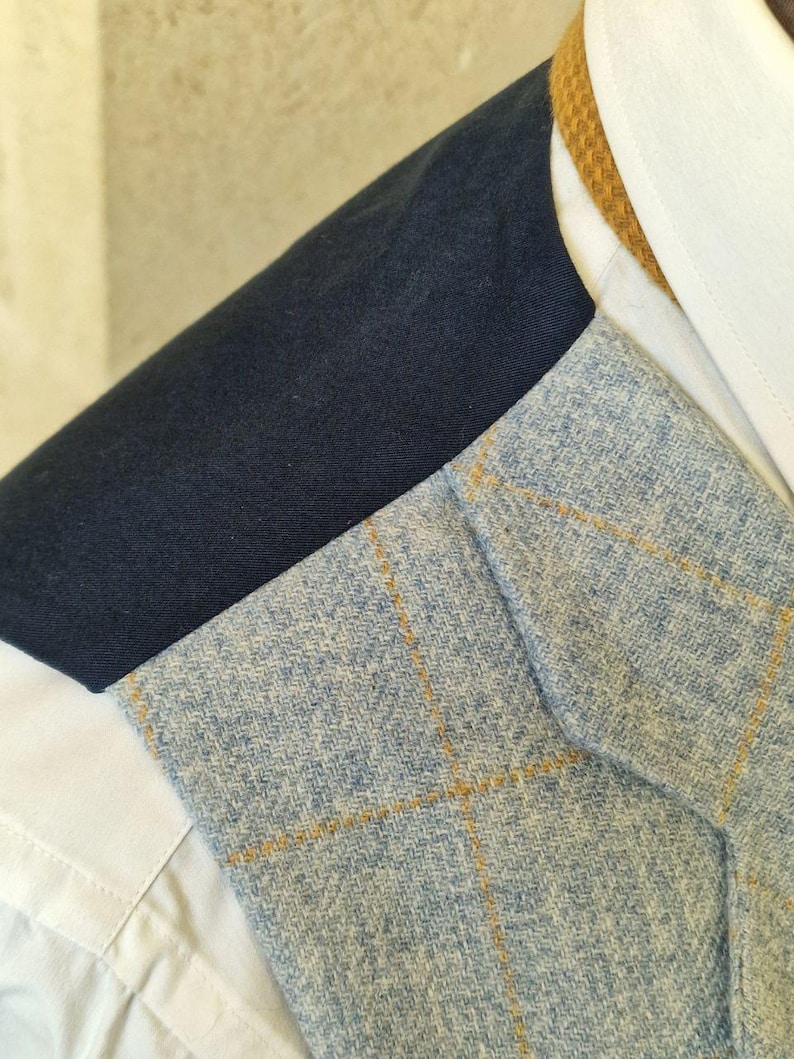 K&ouml;nnte beinhalten: Nahaufnahme eines hellblauen Tweed-Blazers mit gelbem Karomuster. Der Blazer ist &uuml;ber einem wei&szlig;en Hemd und einer marineblauen Jacke getragen. Ein hellbrauner Kragen ist sichtbar.
