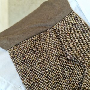 May include: Close-up of a tweed jacket collar with a brown collar and a white shirt underneath. The tweed fabric is a mix of brown, beige, and flecks of red and yellow.