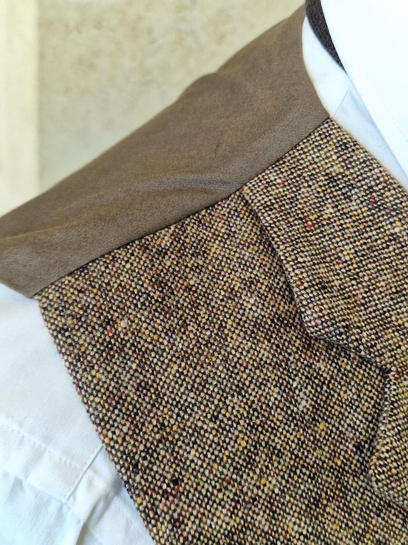 May include: Close-up of a tweed jacket collar with a brown collar and a white shirt underneath. The tweed fabric is a mix of brown, beige, and flecks of red and yellow.