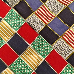 May include: Close-up of patterned fabric featuring a repeating design of squares. The squares display patriotic motifs: red and white stripes, white stars on blue, and alternating solid colors. The squares are outlined with a gold rope-like trim.
