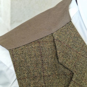 K&ouml;nnte beinhalten: Nahaufnahme einer Tweedweste mit braunem Kragen. Die Weste besteht aus einer Mischung aus gr&uuml;nen, braunen und roten F&auml;den, die ein strukturiertes Aussehen erzeugen. Ein wei&szlig;es Hemd ist darunter zu sehen, was auf formelle oder Business-Kleidung hindeutet.