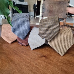 May include: A collection of six patterned neckties in various colors, including peach, navy blue, brown, light gray, and tan. The ties are arranged on a wooden surface, showcasing their textured weave and classic design. The ties are a classic accessory.