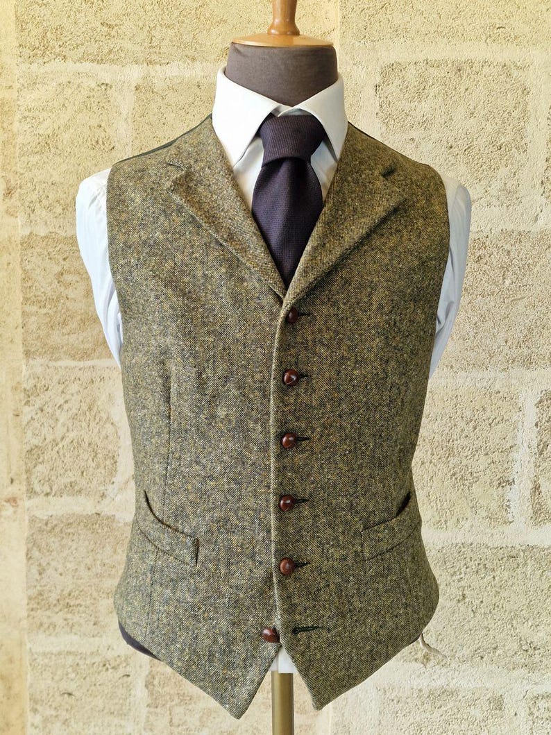 May include: A tweed vest in shades of olive green and brown, featuring a notched lapel, two front pockets, and a button-down closure. The vest is worn over a white dress shirt and a dark tie, creating a classic, tailored look.