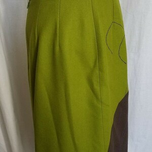 May include: A green skirt with a brown panel on the side. The skirt has a simple design and a straight cut.