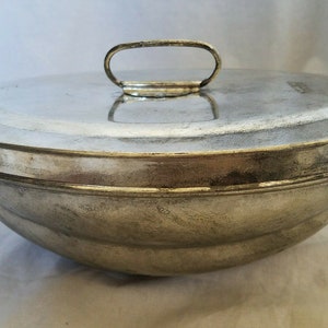 May include: A silver metal bowl with a lid and a handle. The bowl is round and has a smooth surface. The lid is also round and has a smooth surface. The handle is made of metal and is attached to the lid.