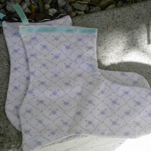 Può includere: Due calze bianche con un motivo floreale blu chiaro e viola e un nastro blu chiaro in cima.