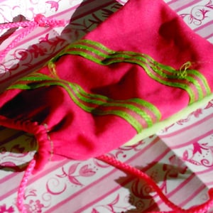 May include: A pink drawstring bag with green ribbon accents. The bag is lying on a white and pink patterned surface.