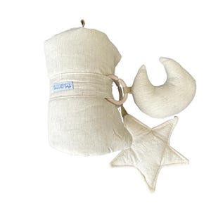 Puede incluir: Un gimnasio de juego para bebés beige con una luna creciente, una estrella y un anillo de madera. El gimnasio está hecho de tela suave y tiene una etiqueta que dice "Sows & Style".