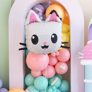 Könnte beinhalten: Ein weißer Ballon in Katzenform mit rosa Ohren und einem lächelnden Gesicht, umgeben von einer Ansammlung pastellfarbener Ballons. Die Ballons sind in einem Torbogen angeordnet und schaffen eine festliche und verspielte Szene, ideal für eine Geburtstagsfeier.