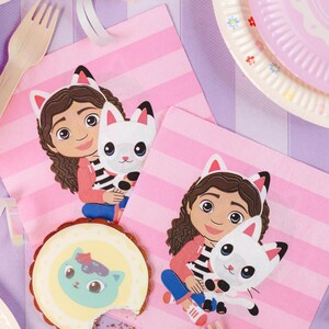 Könnte beinhalten: Party-Dekoration mit einem Cartoon-Mädchen mit Katzenohren, das eine weiße Katze hält. Rosa gestreifte Servietten, ein dekorierter Keks und ein rosa Teller sind ebenfalls zu sehen. Thema: Kindergeburtstagsparty.