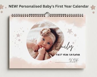 May include: A wall calendar with a spiral binding featuring a central circular photo of a baby wearing a floral headband. The background is a soft peach watercolor wash with small star illustrations. Text reads: NEW! Personalised Baby's First Year Calendar, Emily, FIRST YEAR CALENDAR, and 2027.