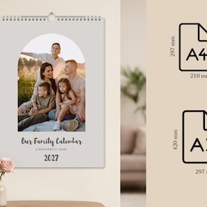 May include: A wall calendar with a spiral binding featuring a family photo inside an arch-shaped frame. The text reads Our Family Calendar, A WONDERFUL YEAR!, and 2027. Size options include A4 at 210 mm by 297 mm and A3 at 297 mm by 420 mm.