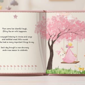 May include: An open children's book with a pink cover featuring a watercolor illustration of a rabbit on a swing under a pink tree. The text reads: Then came her cheerful laugh, filling the air with happiness. She enjoyed listening to stories and songs.