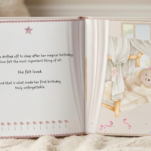 May include: An open children's storybook with a light pink color scheme. The left page features text about a first birthday and feeling loved. The right page shows an illustration of a small bunny sleeping in a canopy bed with pink balloons.