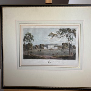 May include: Framed antique print of a stately home in a landscape. The artwork features a large white building with multiple windows, surrounded by trees and a grassy field. The print is in a black and gold frame.