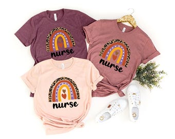 May include: Three t-shirts with a rainbow design and the word "nurse" printed on them. The rainbow is made of different colors and has a leopard print pattern. The t-shirts are in different colors: maroon, pink, and light pink.