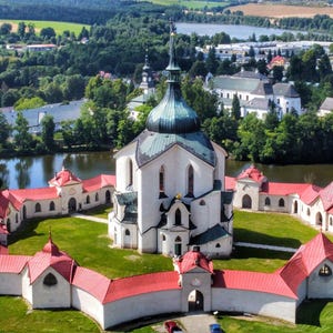 May include: An aerial view of a white church with a green dome and red roofs. The church is surrounded by a moat and a lush green lawn. The church is located in a rural area with trees and a lake in the background.
